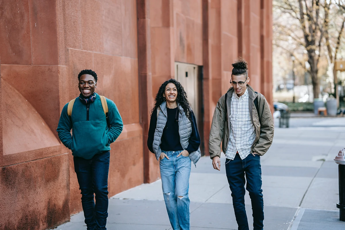 A group of 3 students walk along a sidewalk smiling and laughing