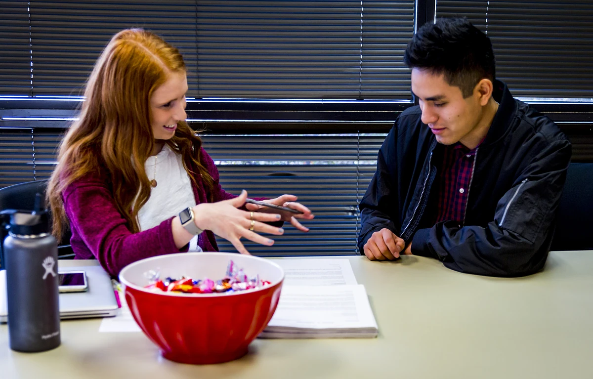 Two people are having a conversation at a table with a bowl of candy and documents.